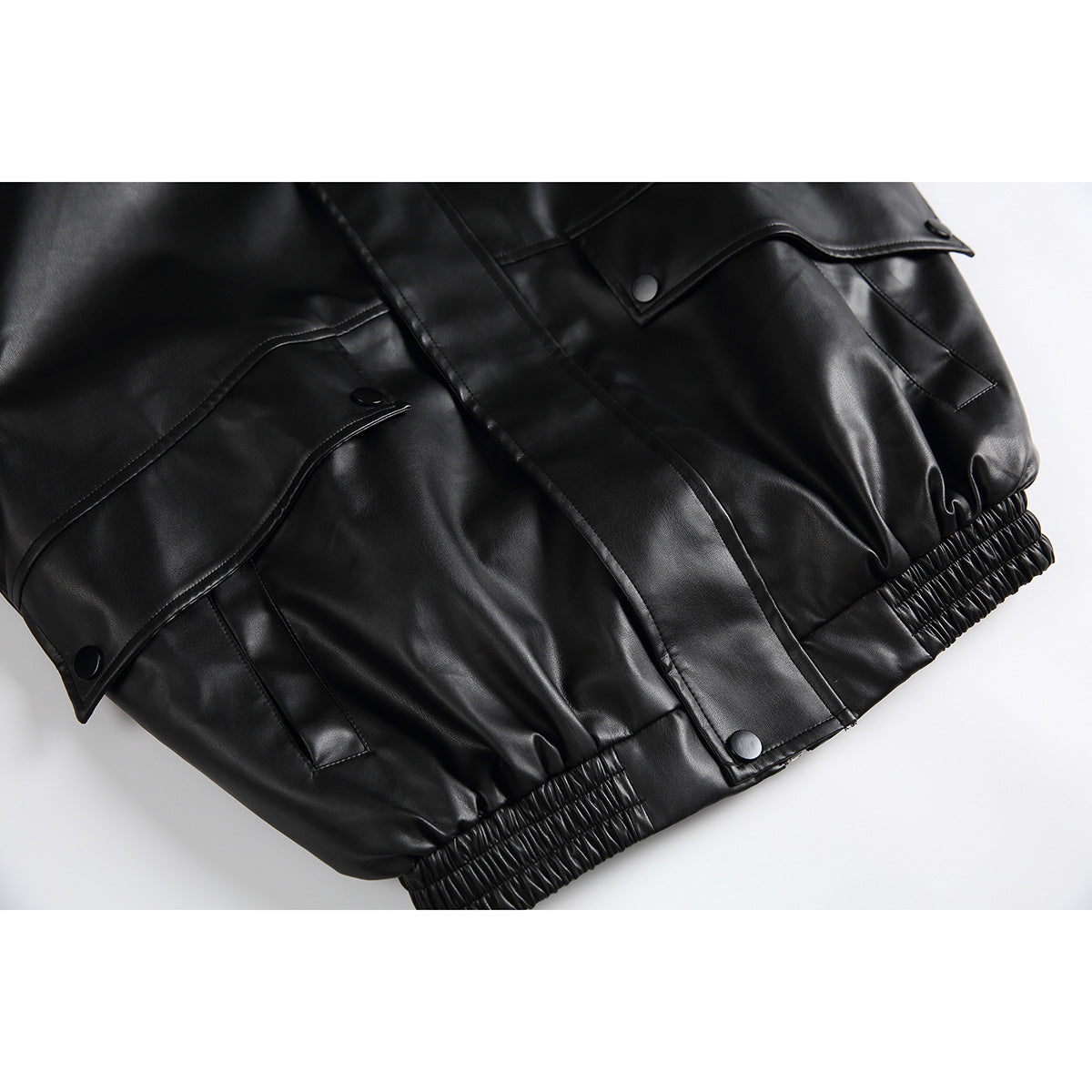 Close-up of a black jacket's flap pockets, snap buttons, covered front placket, and gathered elastic hem.