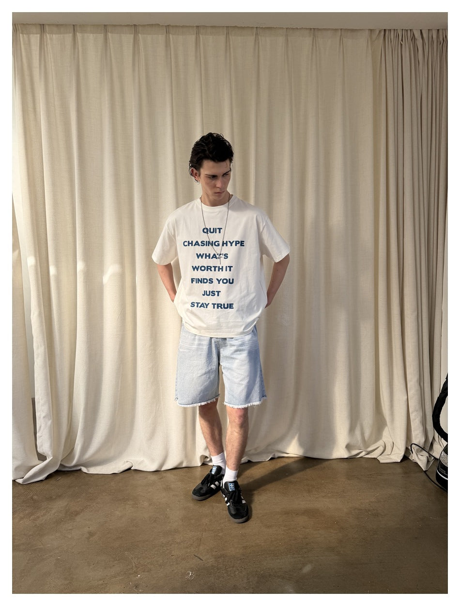Model wearing a white T-shirt with blue front lettering and light blue cutoff denim shorts.