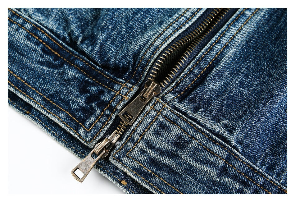 Close-up of a metal zipper and reinforced seams on faded blue denim.
