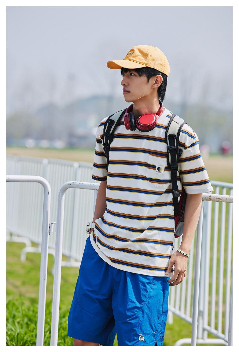 Model wearing a white striped T-shirt with a chest pocket and bright blue shorts, shown from the front at an angle.