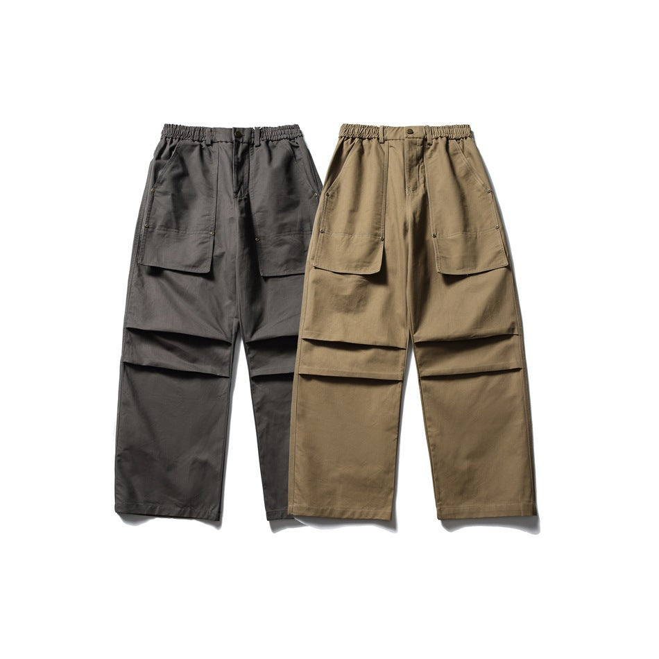 Two pairs of wide-leg utility trousers shown from the front in charcoal and olive-brown, with large patch pockets.