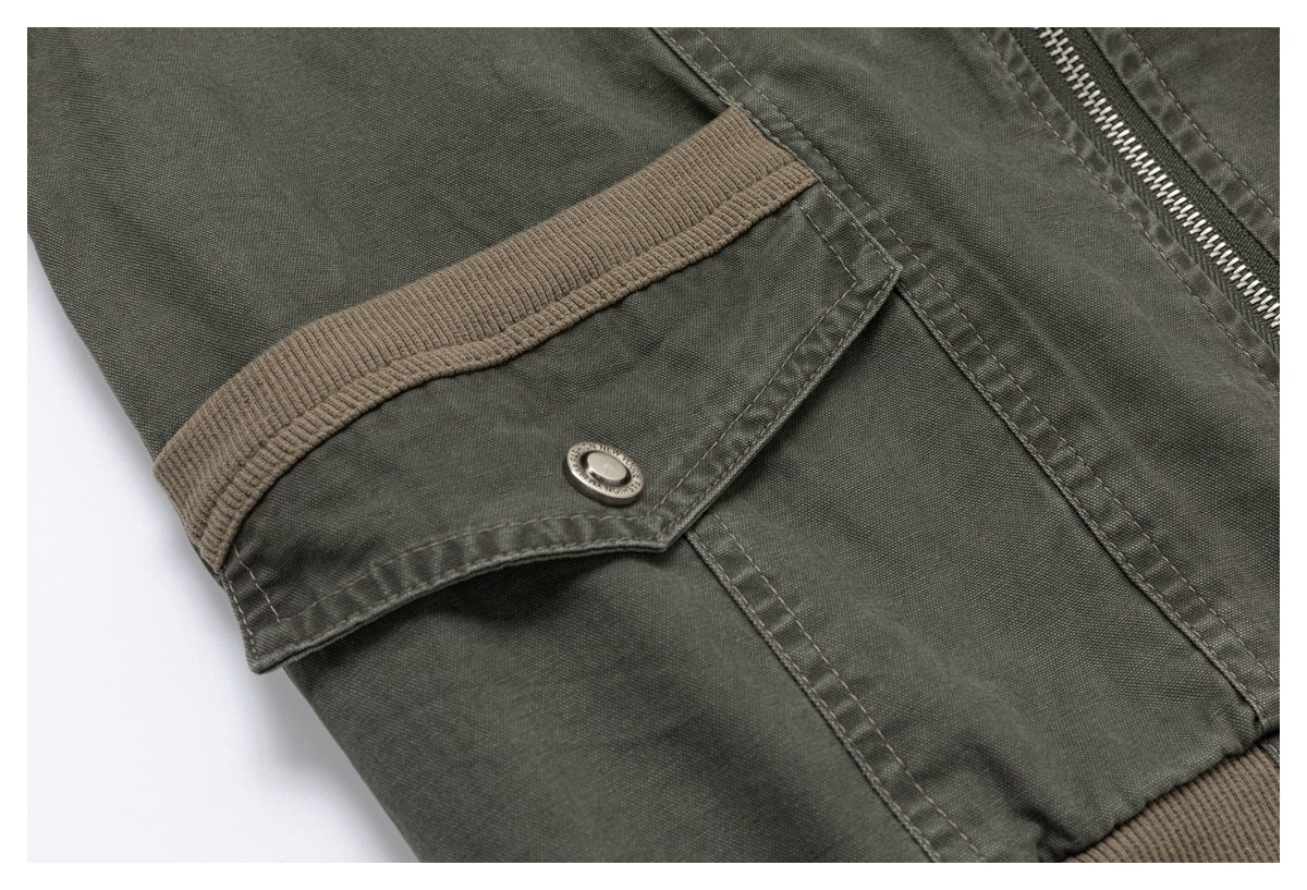 Close-up of an olive-gray jacket pocket flap with a metal snap, zipper, and taupe ribbed trim.