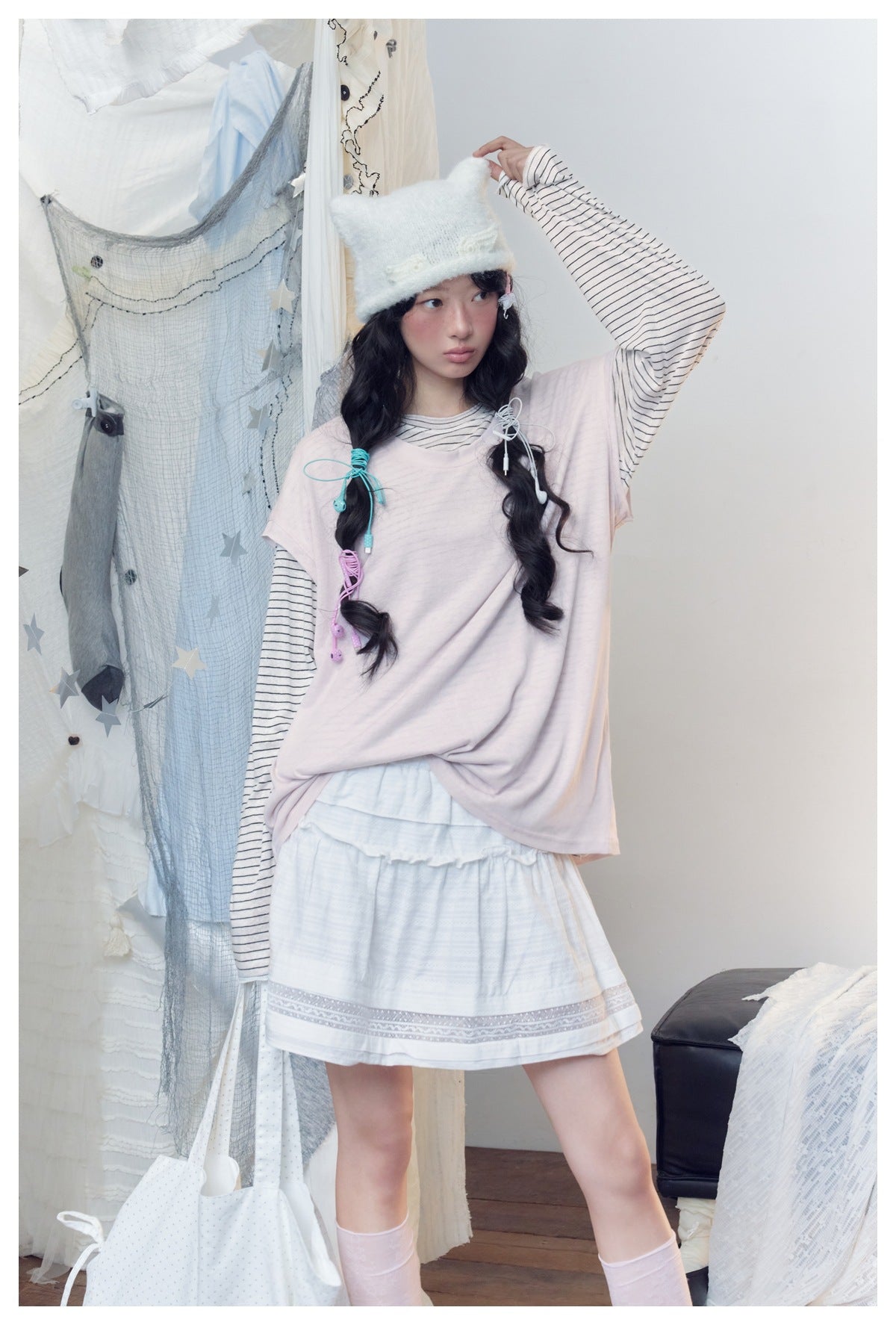 Model wearing a loose pale pink top over a striped long-sleeve shirt and a white skirt with a decorative hem.