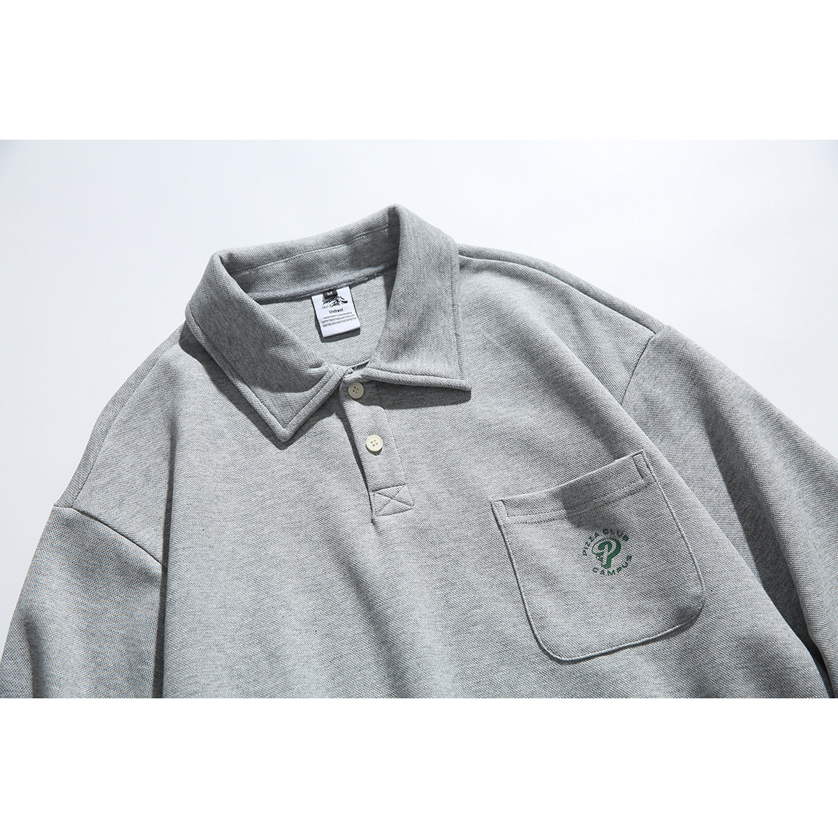 Close-up of a heather gray collared pullover with a two-button placket and small embroidered chest-pocket emblem.
