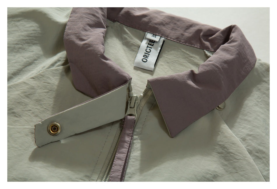 Close-up of a pale sage jacket collar and zipper with mauve trim, a snap tab, and a sewn-in label.