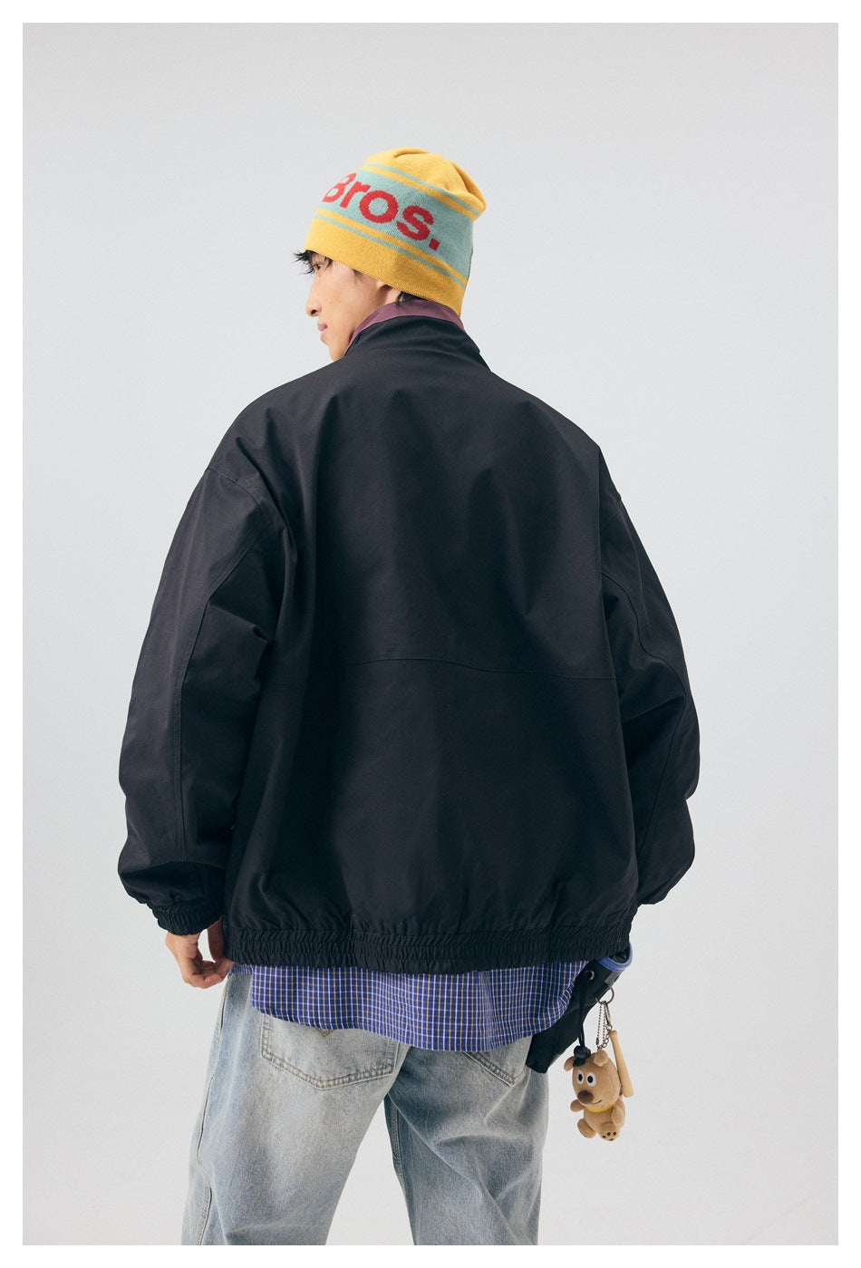 Back view of a model wearing a black jacket with an elastic hem and cuffs; plum collar lining is visible.