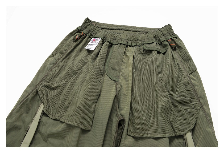 Upper front of an olive-green garment with an elastic waistband, layered mesh panels, pockets and attached tags.