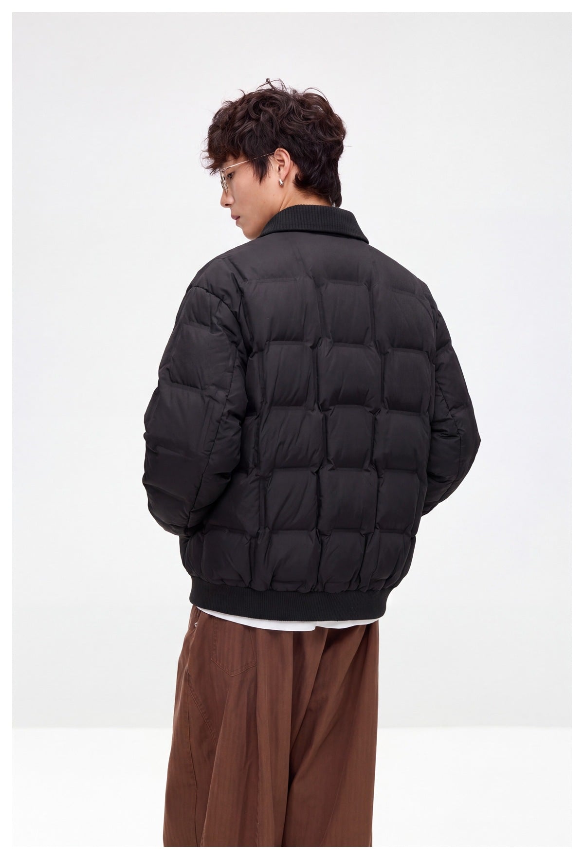 Back view of a model wearing a dark quilted jacket with a ribbed collar and hem.