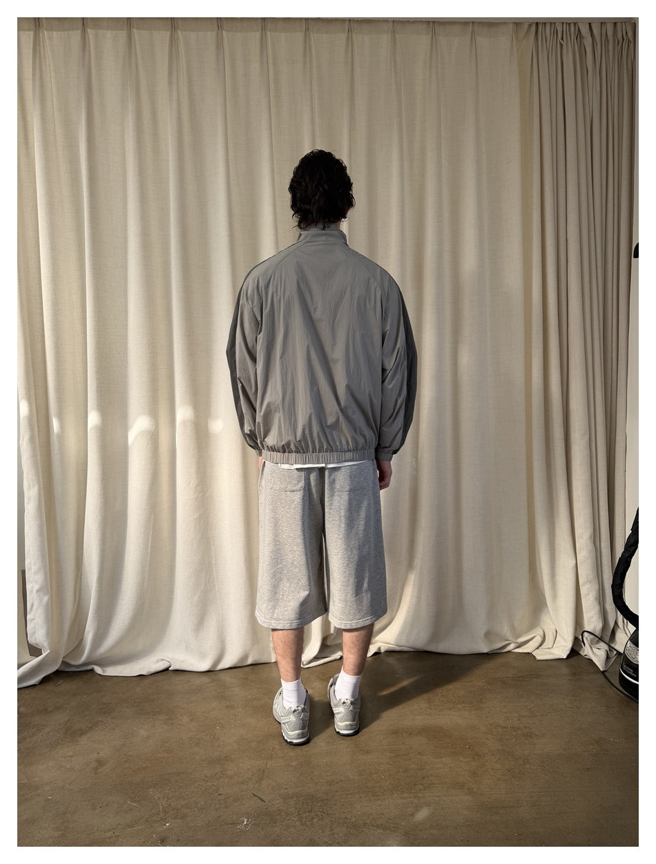 Full-length rear view of a model wearing a light gray jacket with dark shoulder panels and an elastic hem.