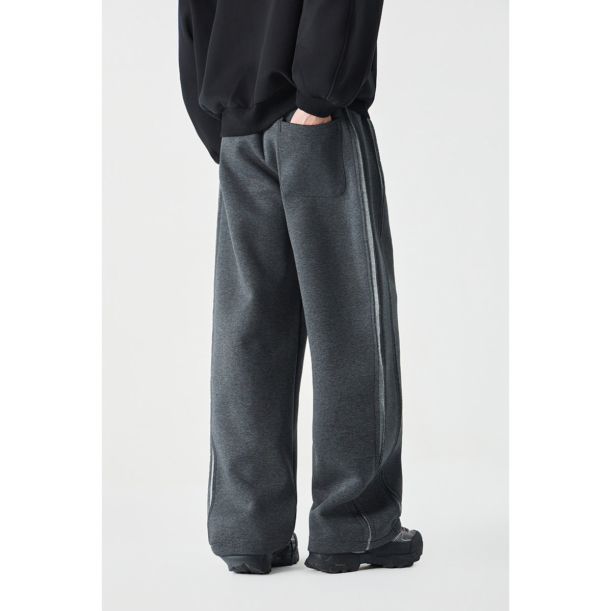 Rear view of a model wearing charcoal wide-leg pants with a back patch pocket and long side seams.