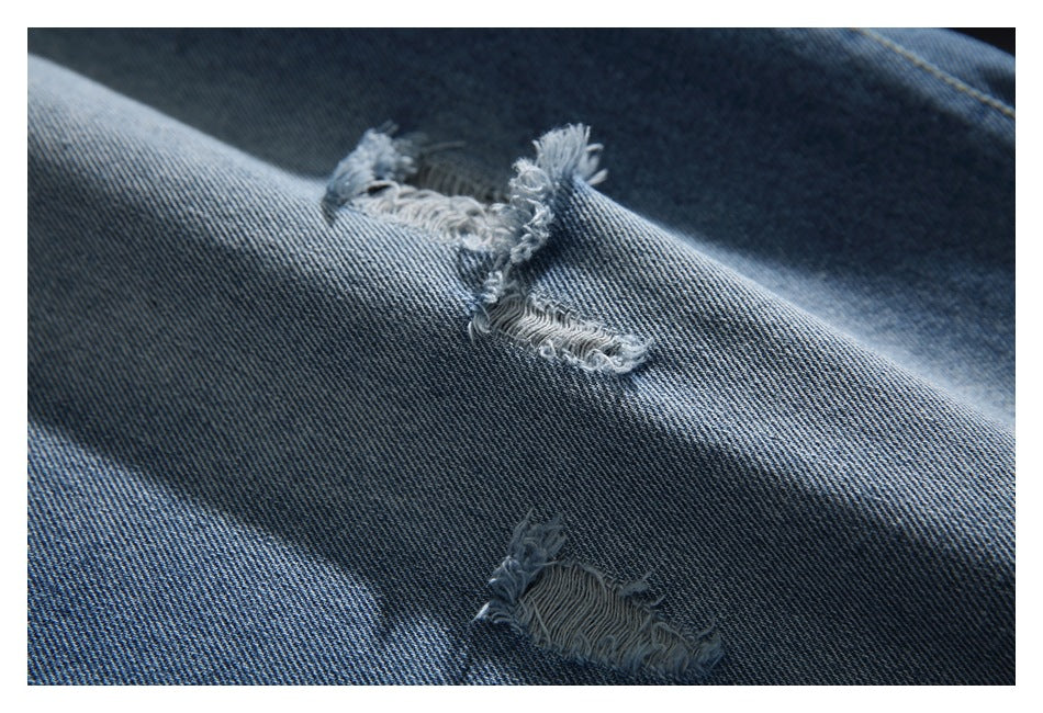 Close-up of distressed blue denim with several frayed ripped patches.