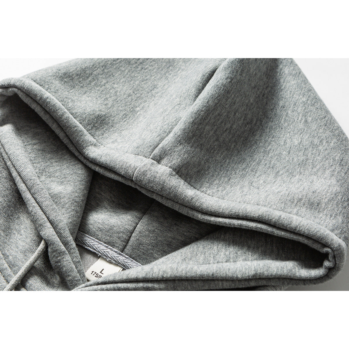 Close-up of the inside seam and gray fabric of a hoodie, with a small size label visible.
