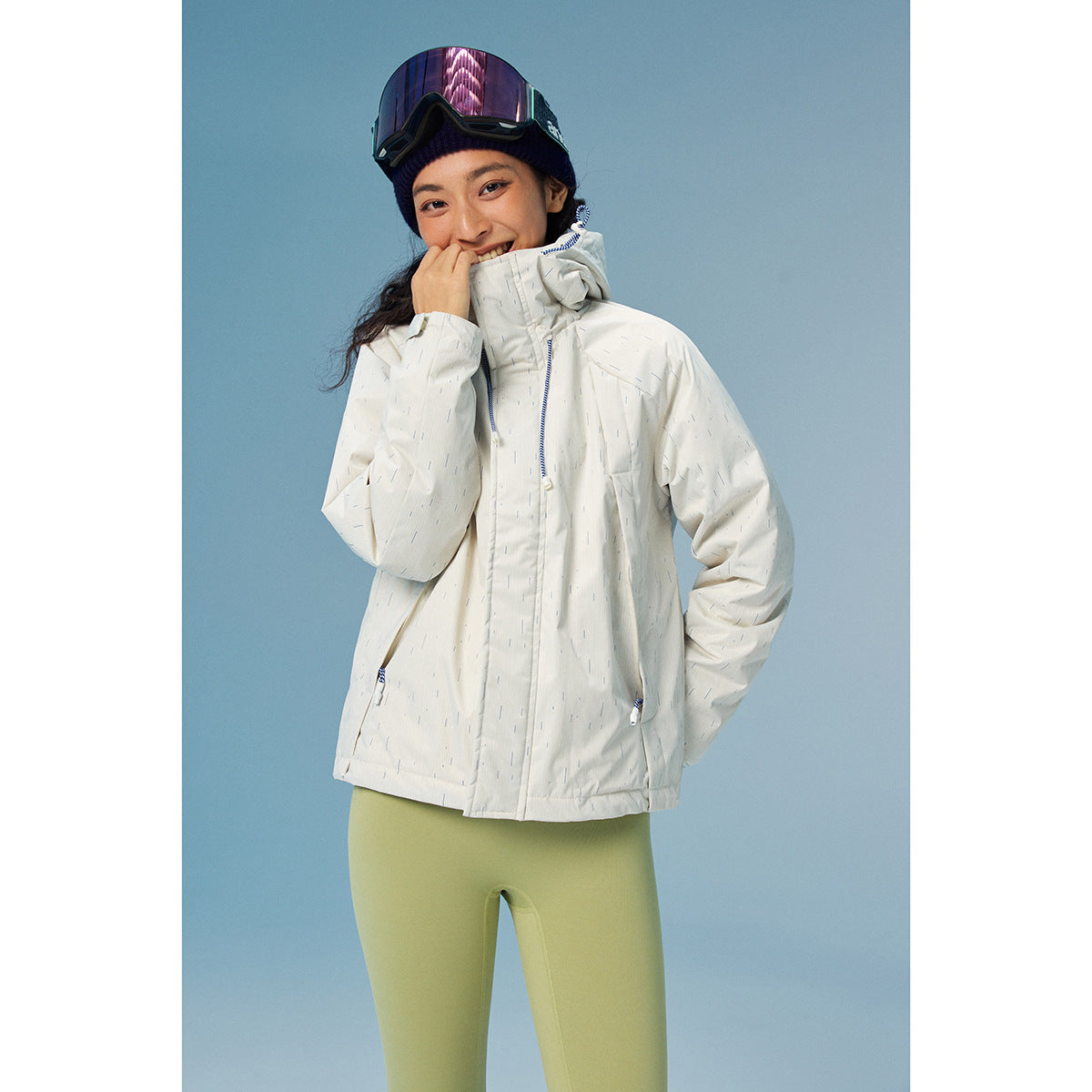 Woman models a white speckled hooded jacket with blue zipper details and light green leggings.