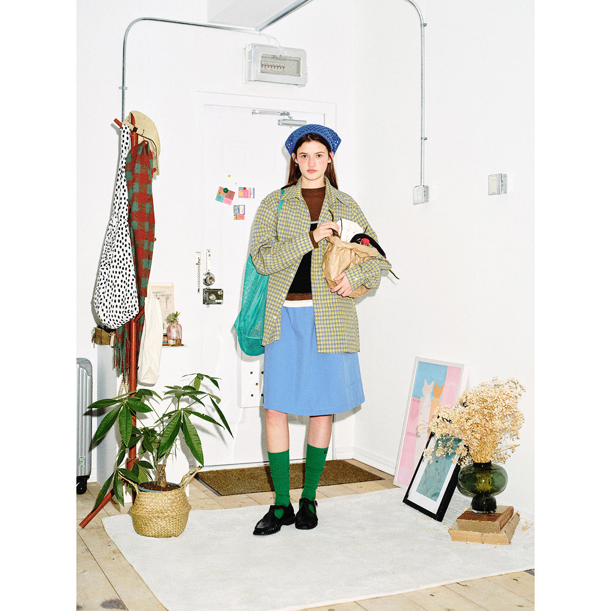 Model wearing a yellow-and-blue plaid button-up shirt, blue skirt, green socks and blue knit beret.