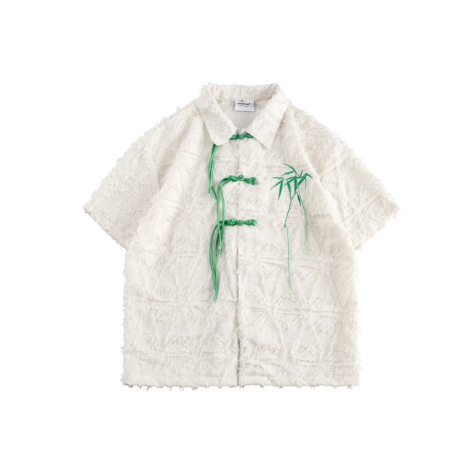Beige short-sleeve textured shirt with green knotted frog closures and embroidered bamboo, flat lay front view