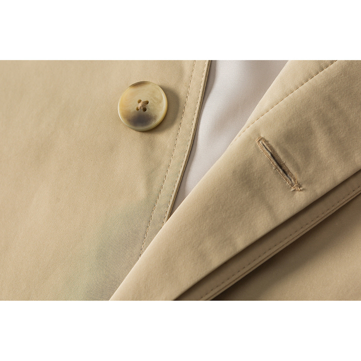 Close-up of a tan coat lapel with a round button, stitched buttonhole, and pale lining.