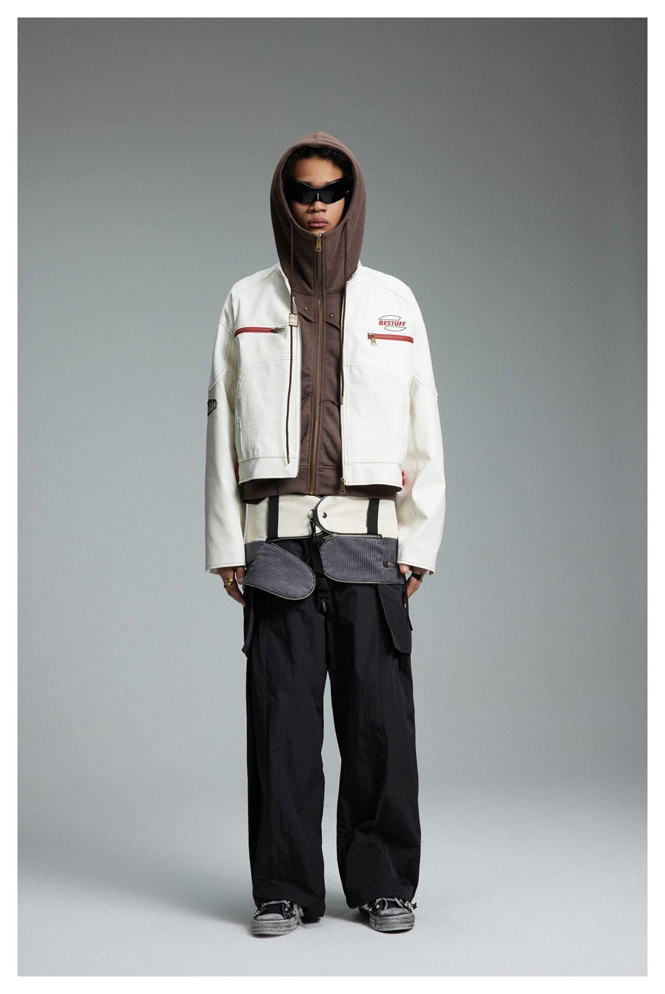 Model wearing the cropped white jacket open over a brown hoodie with black wide-leg pants, front view