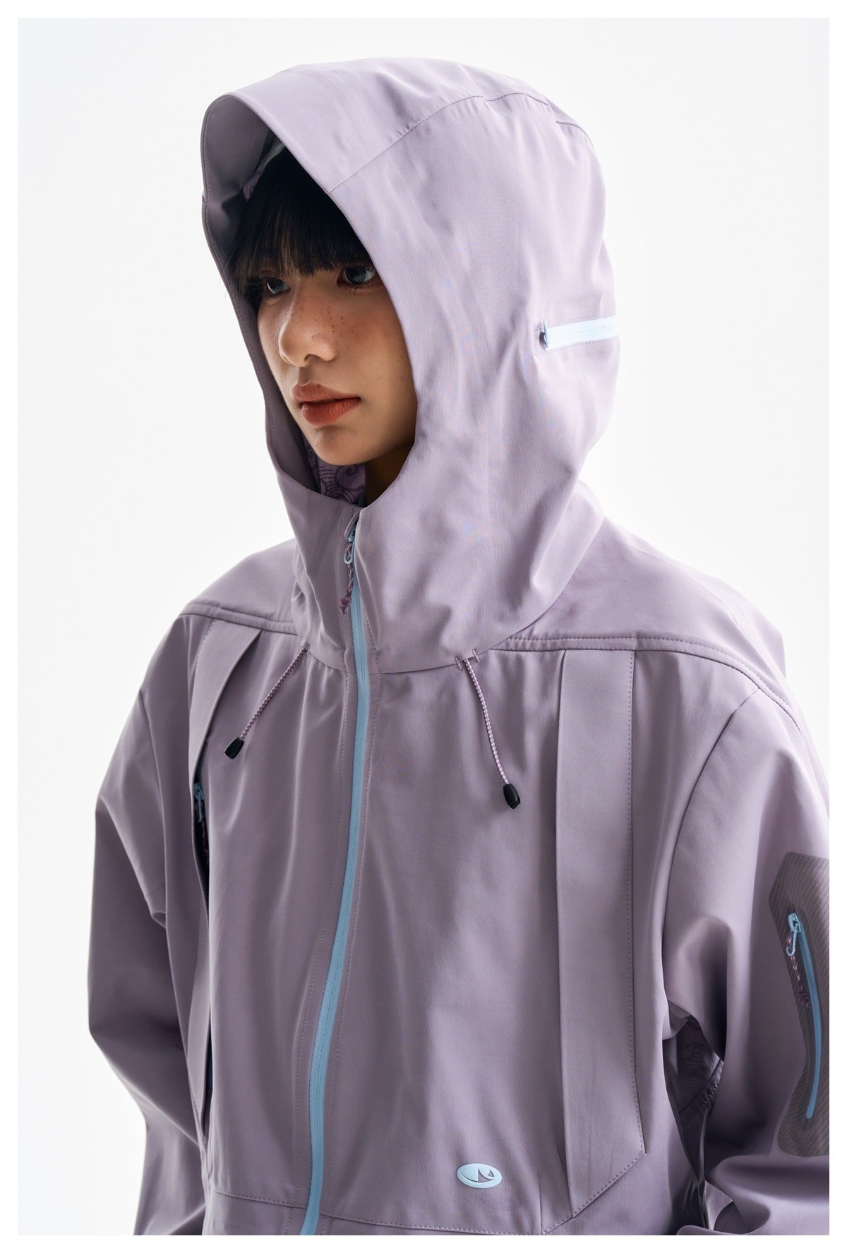 Close-up of a model wearing a lavender hooded jacket with a light blue zipper and sleeve pocket.