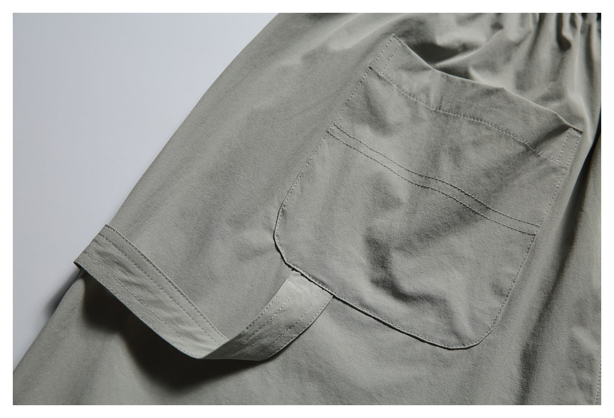 Close-up of a gray garment showing a stitched patch pocket and double-stitched edge.