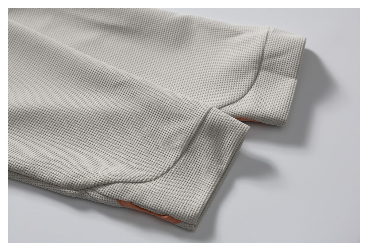 Close-up of a pale gray waffle-knit garment with a wide stitched cuff and a glimpse of peach fabric beneath.