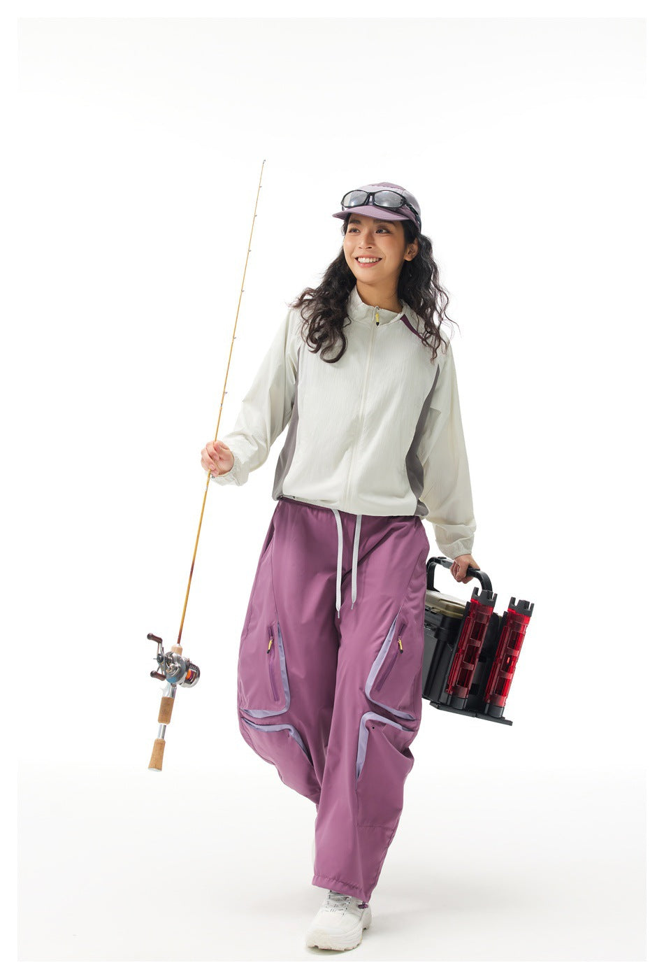 Woman wearing a white zip-up jacket and loose purple cargo trousers, holding fishing gear.