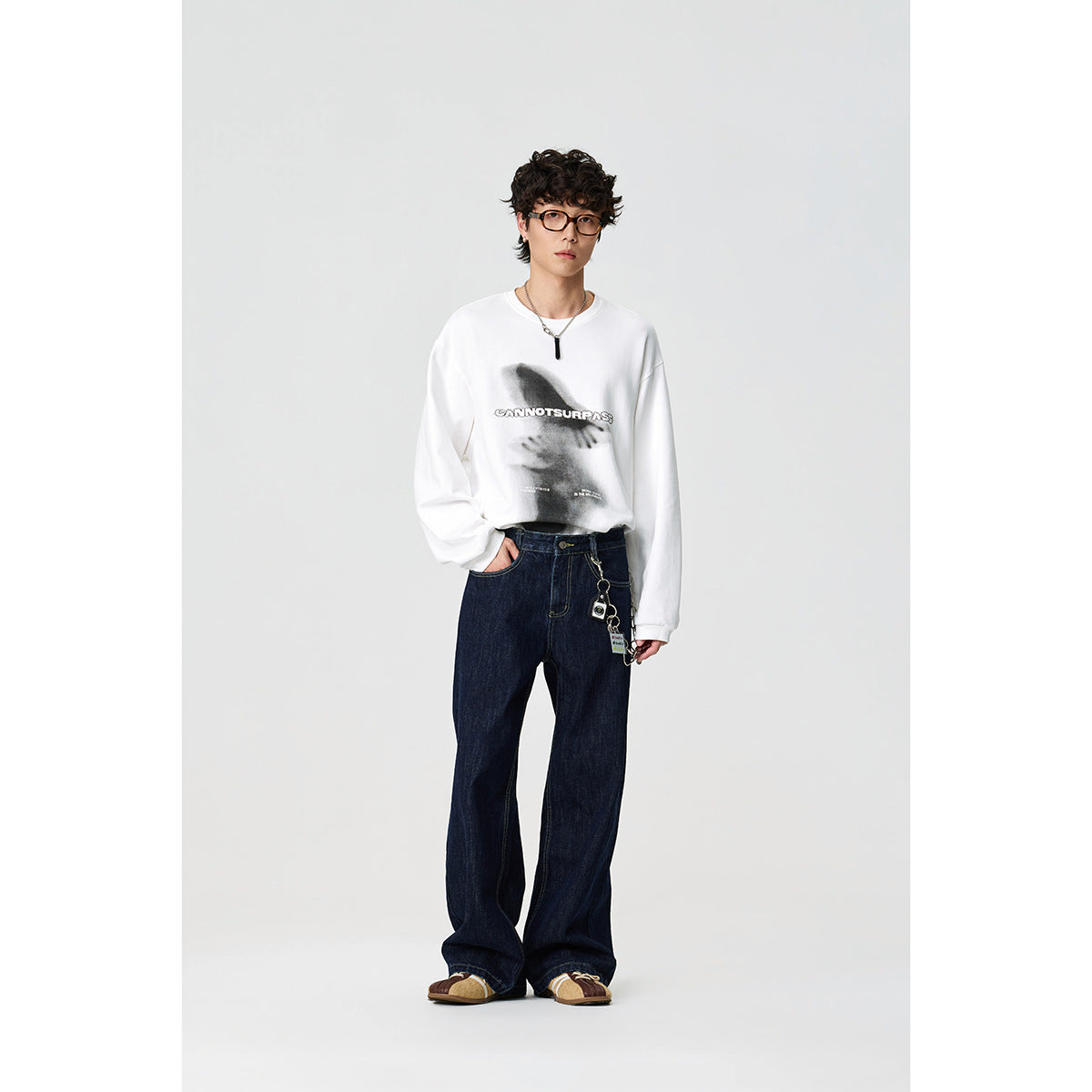 Model wearing a white long-sleeve graphic shirt with dark wide-leg jeans; front view.