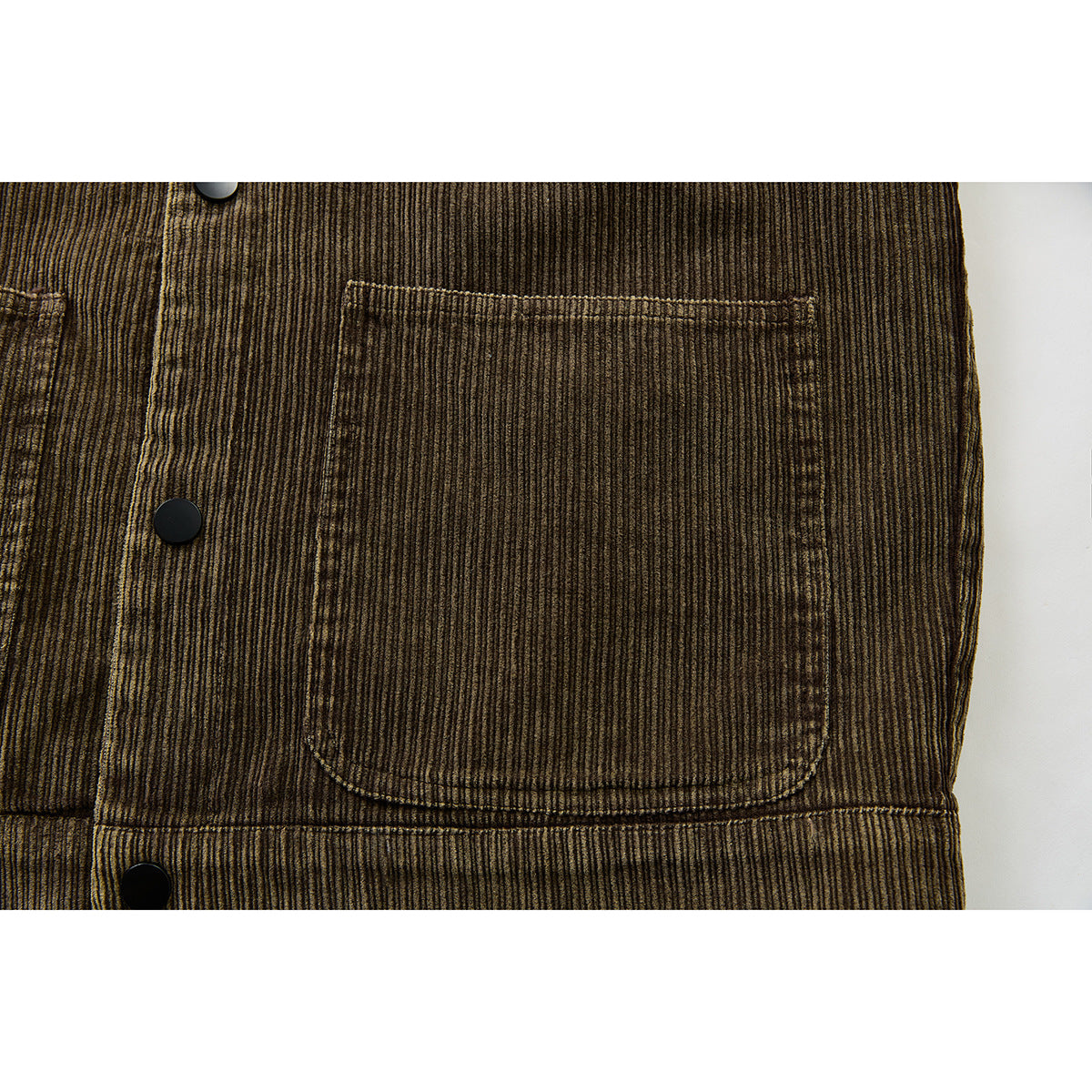 Close-up of a patch pocket and black snap buttons on the brown corduroy jacket front.