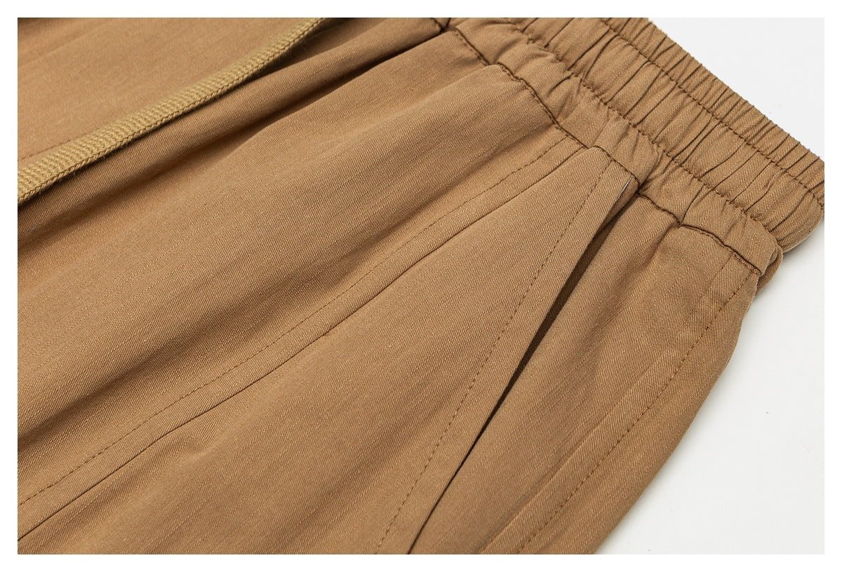Close-up of tan trousers showing the elastic waistband, drawstring, and side pocket opening.