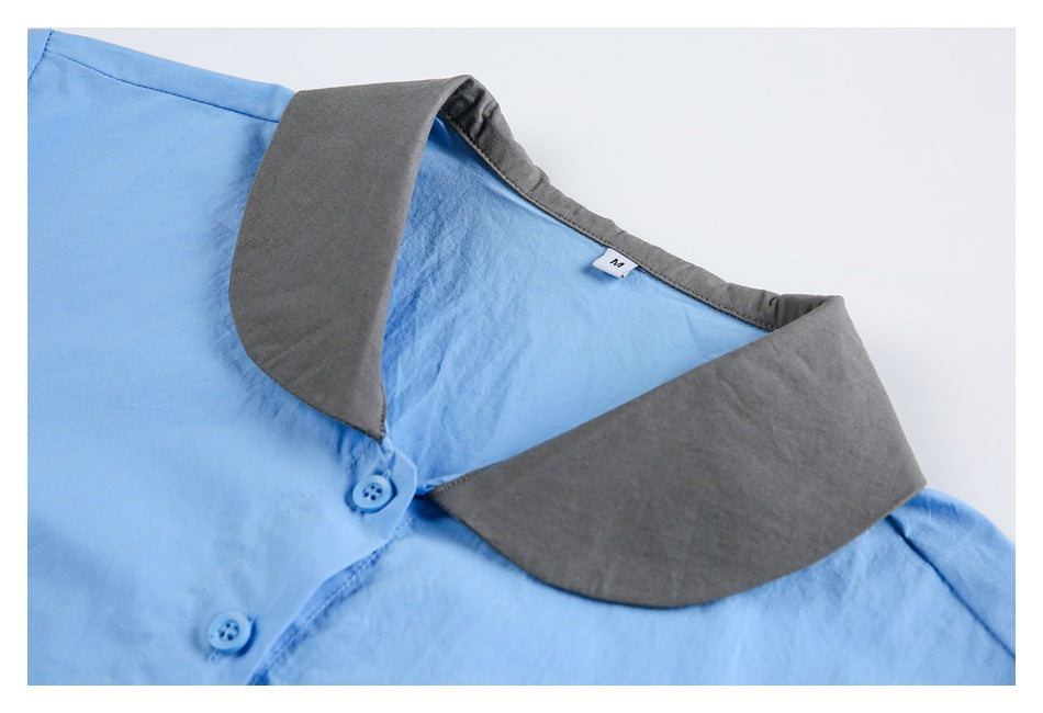 Light blue shirt laid flat, showing its broad charcoal gray collar and blue buttons.