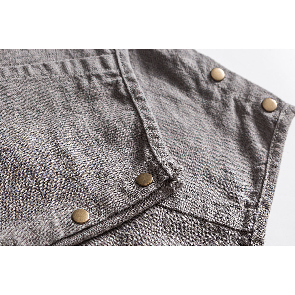 Close-up of gray trousers showing brass-tone snap buttons, stitched seams, and a folded cuff.