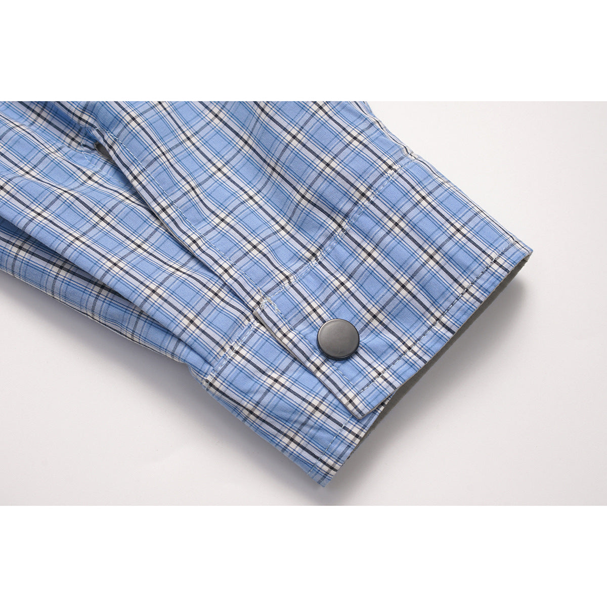 Close-up of a blue plaid shirt sleeve with a buttoned cuff.