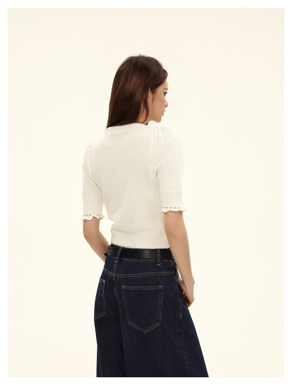 Back view of a model wearing the white cropped knit top, showing its plain back and scalloped sleeve edges.