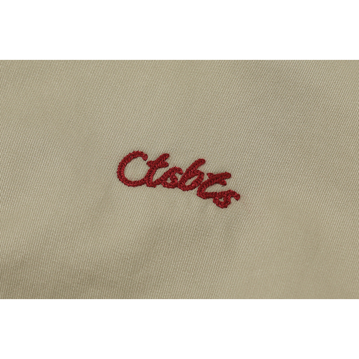 Close-up of red cursive embroidery on khaki fabric.