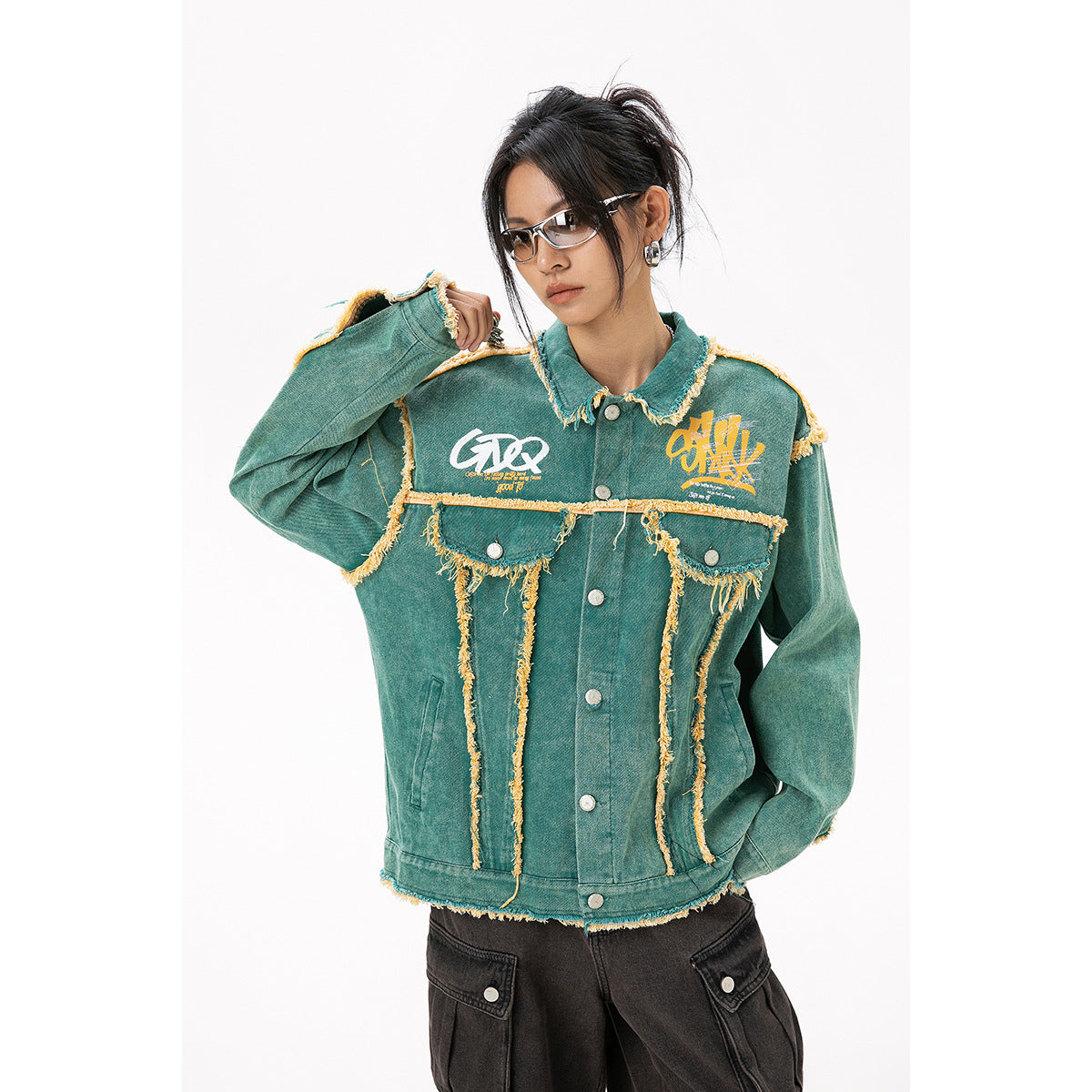 Model wearing a teal jacket with yellow frayed trim, chest graphics, flap pockets, and silver buttons.