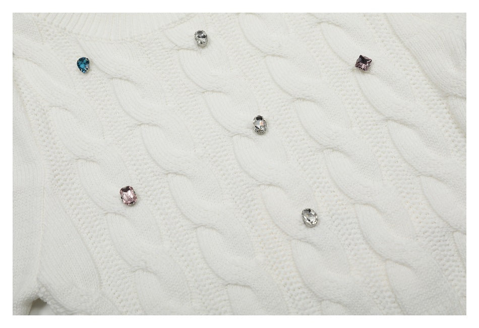 Close-up of white cable-knit sweater stitching with scattered blue, pink, and clear jeweled accents.