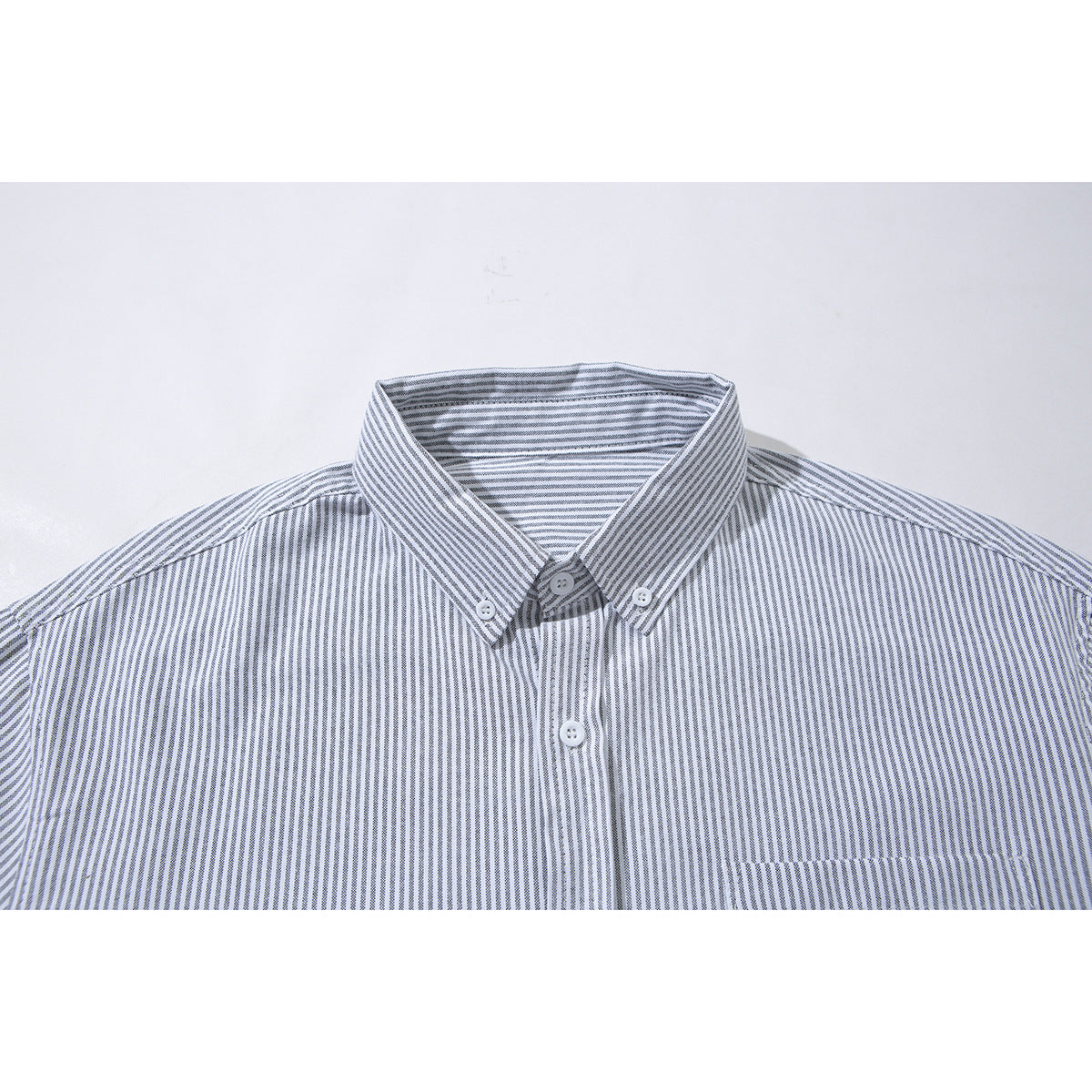 Close-up of a white shirt with fine gray vertical stripes, showing its button-down collar and upper chest.