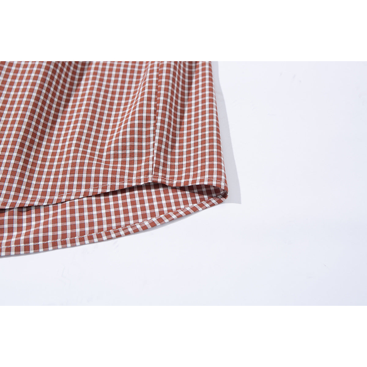 Close-up of the rust and white gingham shirt’s curved hem and stitched edge.