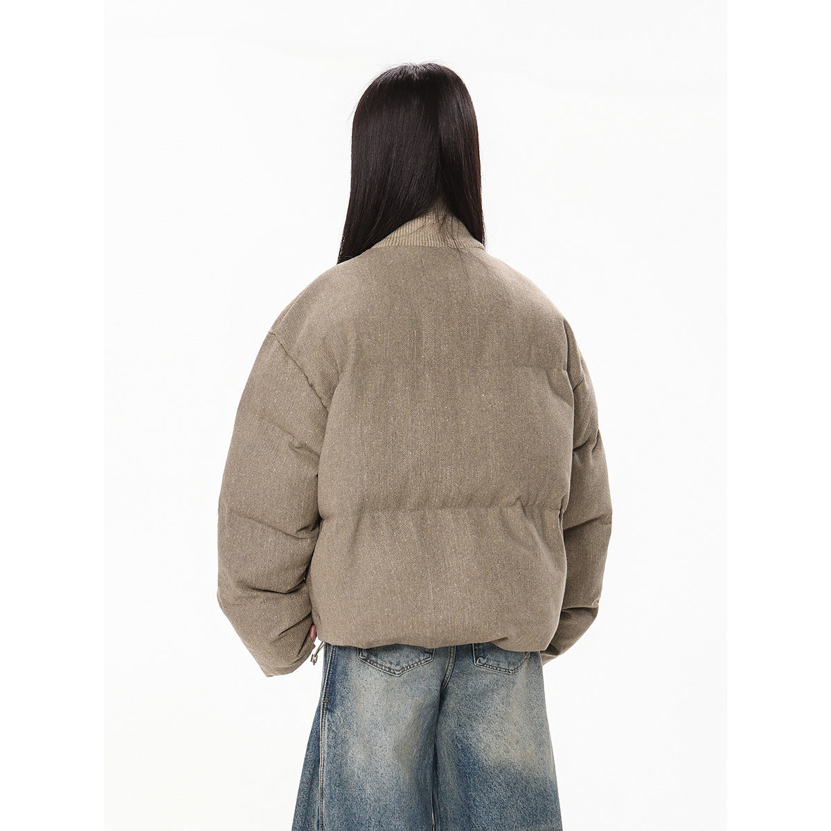 Back view of a model wearing a taupe padded jacket with a high collar and loose blue jeans.
