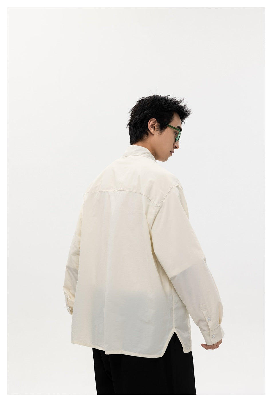 Rear view of a model wearing an oversized ivory shirt with a back yoke and side hem slit.