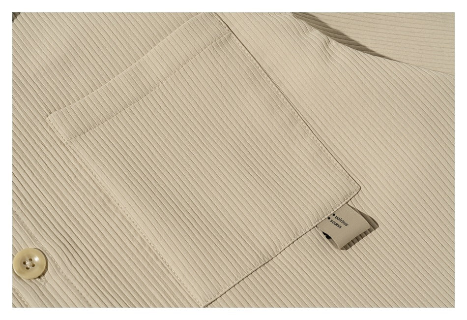 Close-up of the chest pocket and button on a beige ribbed shirt.