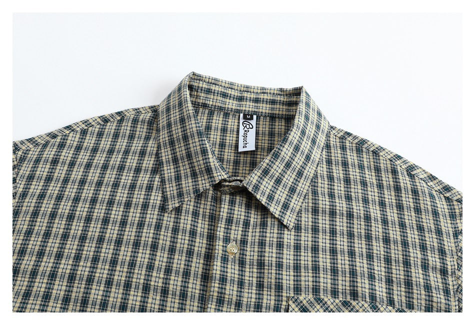 Cropped front view of a beige and navy plaid button-up shirt with a pointed collar and chest pocket.