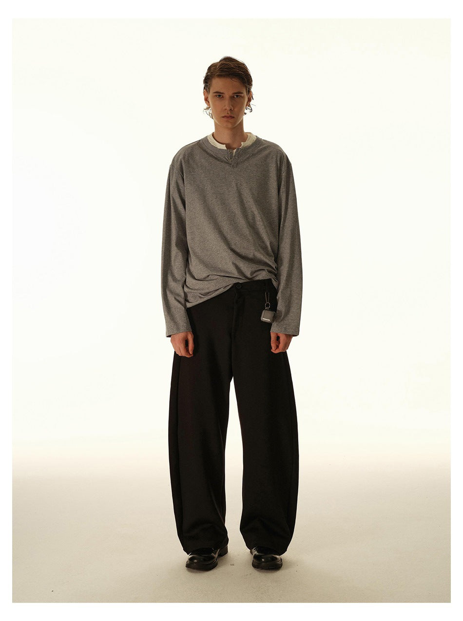 Full-length front view of a model wearing a gray long-sleeve henley and wide black trousers.