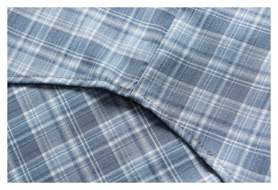 Close-up of a curved stitched hem on a gray-blue plaid shirt.
