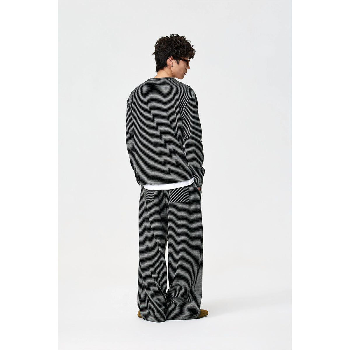 Rear view of a model wearing a black thin-striped henley and matching loose trousers.