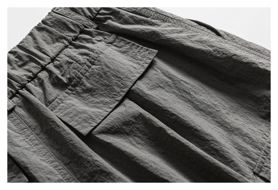 Close-up of a charcoal gray garment showing a large rectangular patch pocket and gathered waist.