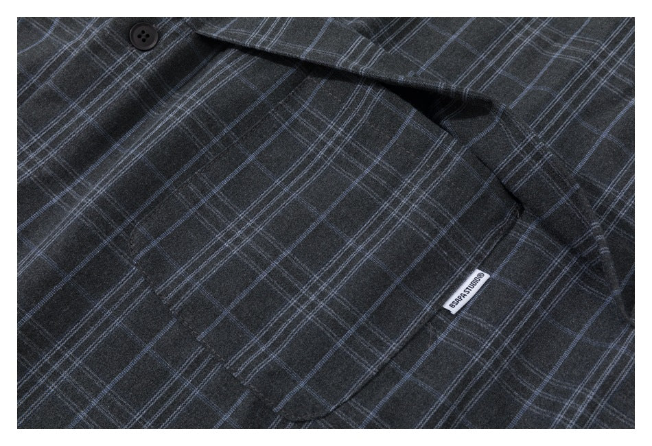 Close-up of a charcoal plaid shirt's chest pocket with a small woven label.