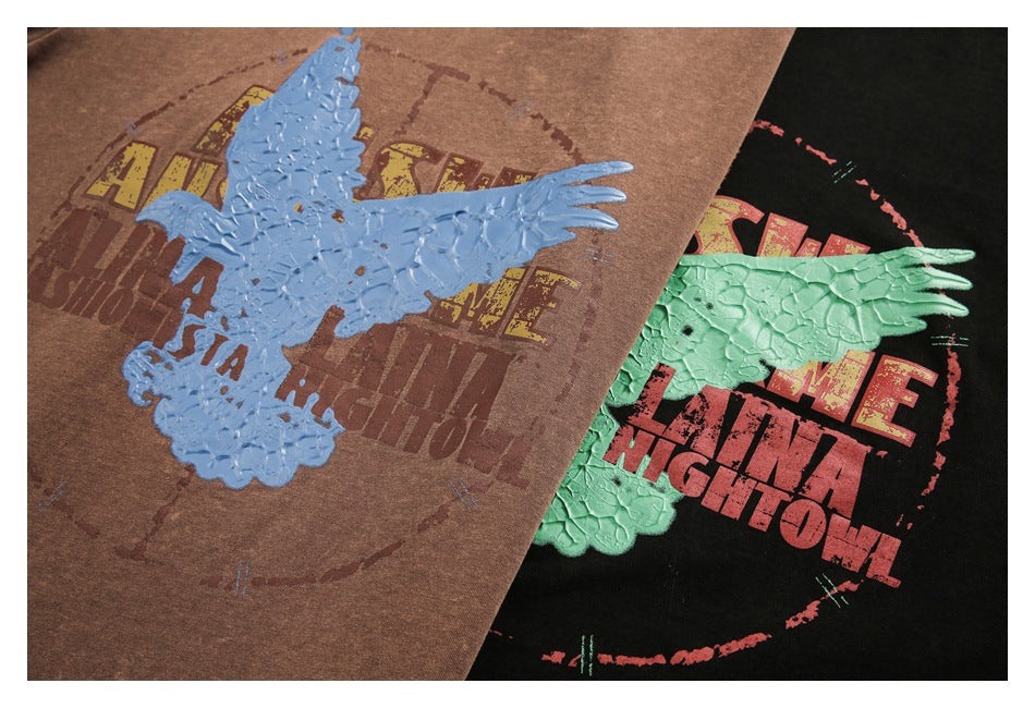 Close-up of brown and black T-shirts with distressed lettering and raised eagle graphics in blue and mint green.