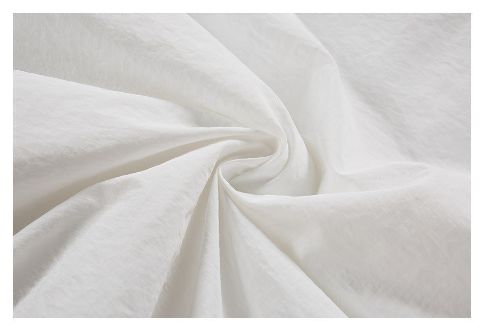 Close-up of white fabric draped in folds, showing a faint grid-like texture.