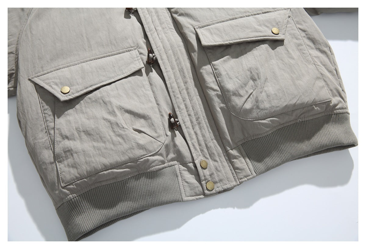 Lower front of a taupe jacket with two flap pockets, toggle closure, brass-colored snaps, and a ribbed hem.