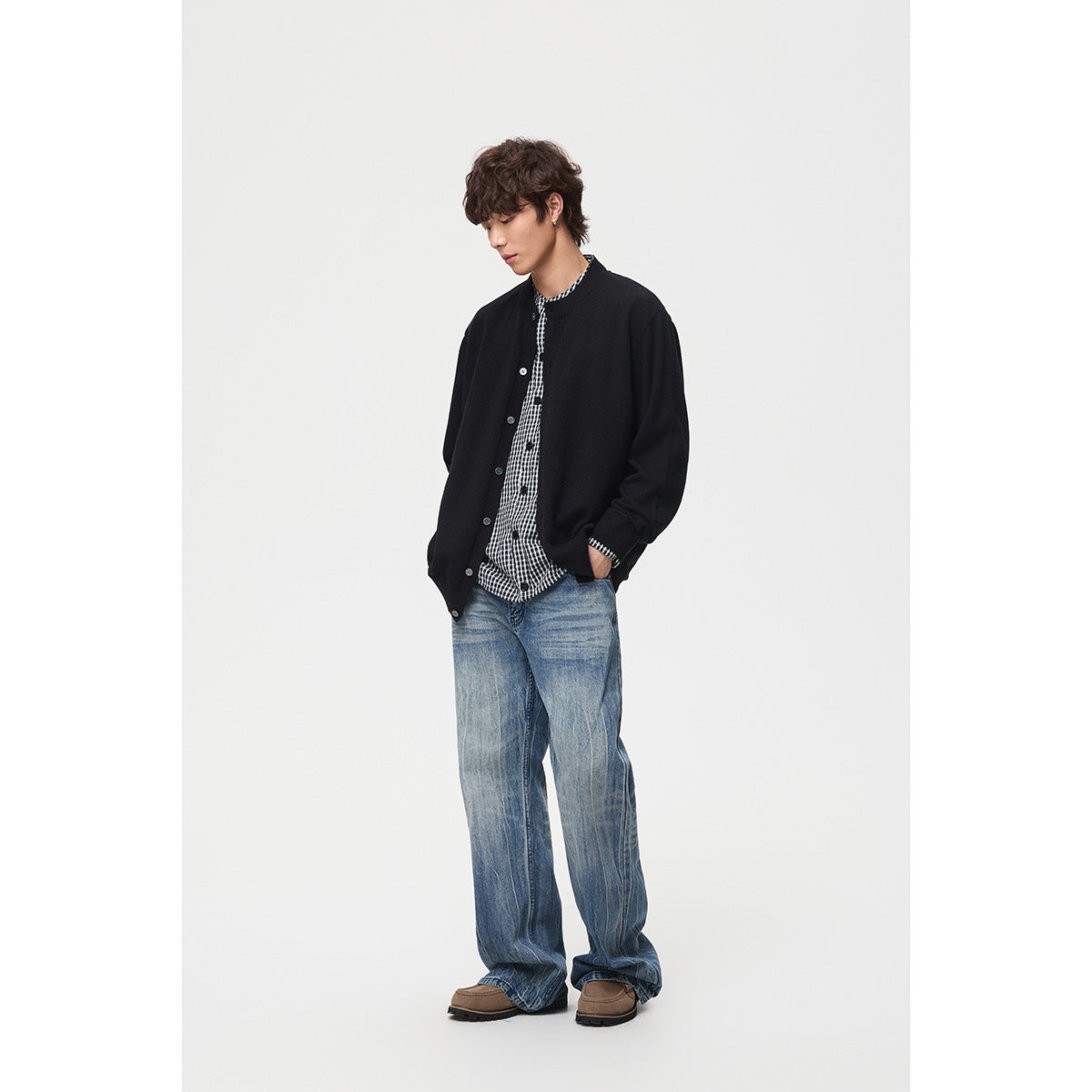 Model wearing a black button-front cardigan over a black-and-white checked shirt with loose blue jeans.